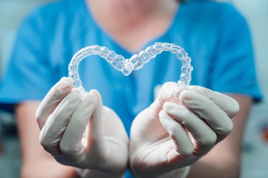 Female,Doctor,Holding,Two,Transparent,Heart-shaped,Dental,Aligners